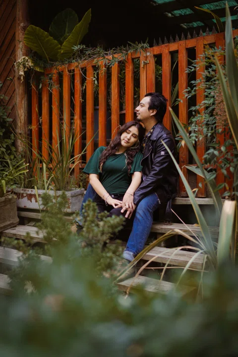 Hombre y mujer están sentados juntos en escalones de madera rodeados de vegetación.
