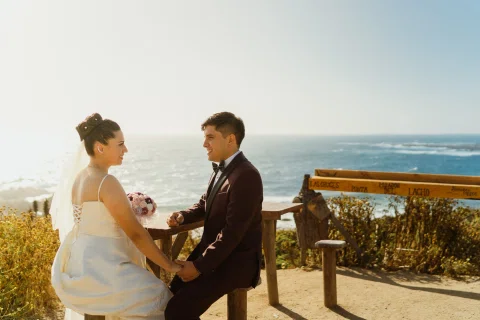 Hombre y mujer están sentados frente al mar y se toman de las manos.