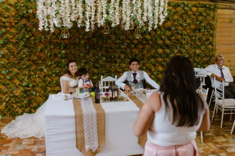 Hombre y mujer están sentados a una mesa con un niño junto a ellos, mientras otra mujer permanece de pie en primer plano.