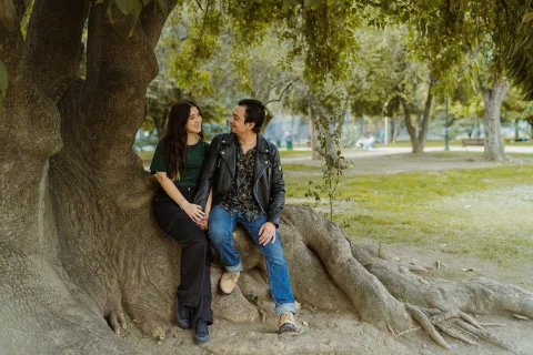 Hombre y mujer están sentados sobre las raíces de un árbol grande mientras se miran.