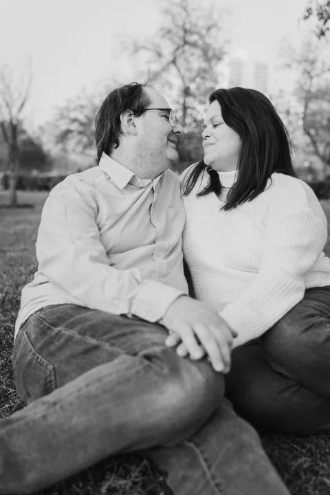Hombre y mujer sentados sobre el césped se miran sonriendo en una fotografía en blanco y negro.