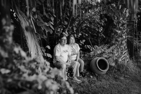 Hombre y mujer sentados a distancia entre abundante vegetación, en blanco y negro.