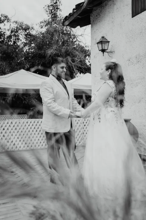 Mujer de cabello rojo con vestido floral y hombre con chaqueta clara se toman de las manos, en una fotografía en blanco y negro.