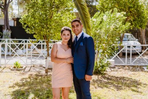 Hombre y mujer con vestimenta formal posan juntos en un jardín arbolado.
