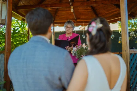 Hombre y mujer vistos de espaldas permanecen frente a una mujer con carpeta dentro de un gazebo.
