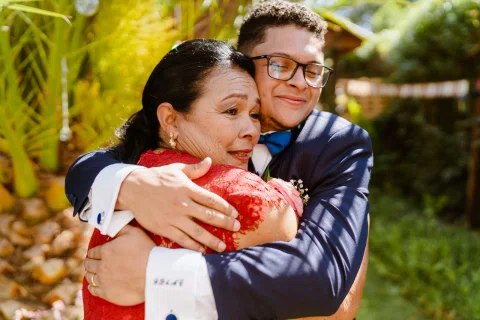 Hombre con traje azul abraza a una mujer con vestido rojo en el jardín.