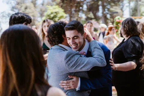 Hombre con traje azul abraza a otro hombre mientras varias personas permanecen alrededor.