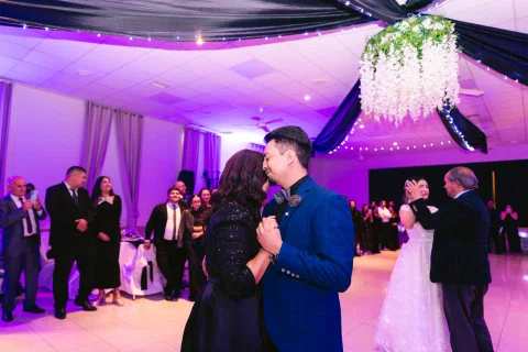 Hombre con traje azul baila con una mujer vestida de negro frente a varias personas.