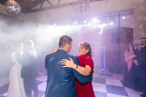 Hombre con traje azul baila con una mujer de vestido rojo bajo luces de escenario.