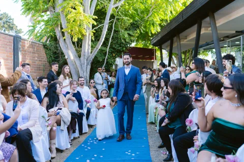 Hombre con traje azul camina por una alfombra azul entre personas sentadas a ambos lados.