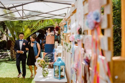 Hombre con traje azul camina del brazo de una mujer junto a una pared decorada con fotografías y cintas.
