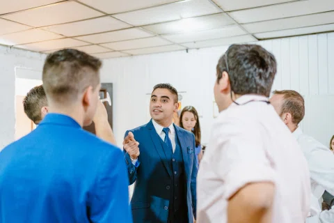 Hombre con traje azul conversa con varias personas en un espacio interior.