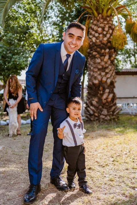 Hombre con traje azul posando junto a un niño pequeño al aire libre.