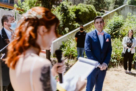 Hombre con traje azul mira a una mujer con vestido blanco que sostiene un micrófono y un documento.