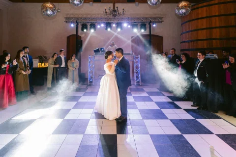 Hombre con traje azul y mujer con vestido blanco bailan abrazados en una pista iluminada.