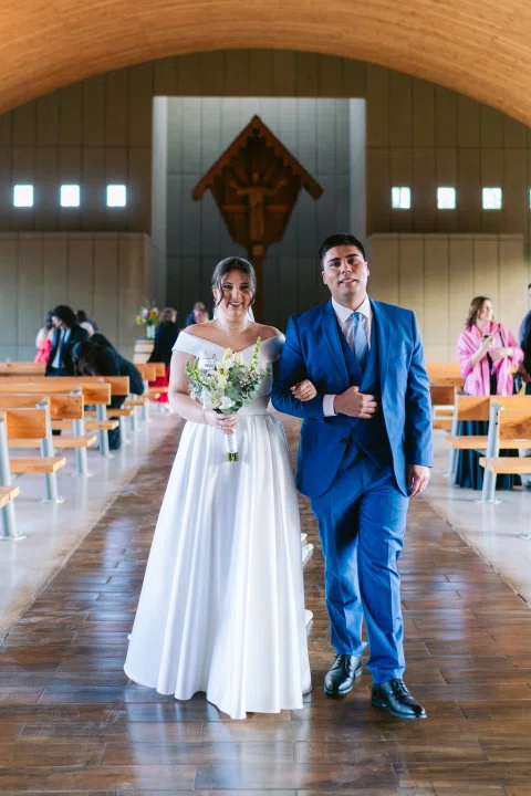 Hombre con traje azul y mujer con vestido blanco caminan juntos por el pasillo interior.
