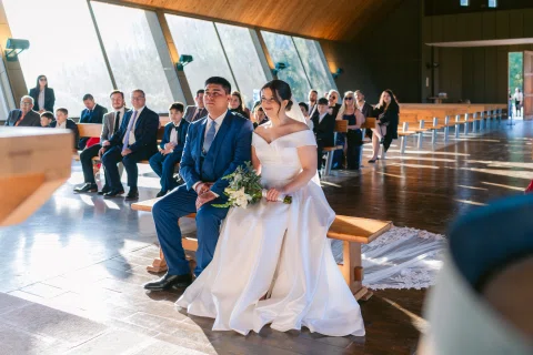 Hombre con traje azul y mujer con vestido blanco están sentados juntos en una banca.