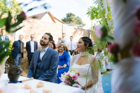 Hombre con traje azul y mujer con vestido blanco están sentados junto a una mesa al aire libre.