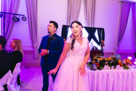 Hombre con traje azul y mujer con vestido blanco sonríen juntos dentro del salón iluminado en violeta.