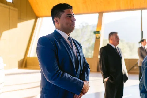 Hombre con traje azul permanece de pie junto al pasillo interior de una capilla.