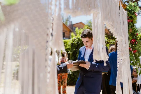 Hombre con traje azul revisa un documento junto a una estructura decorada con tela blanca.