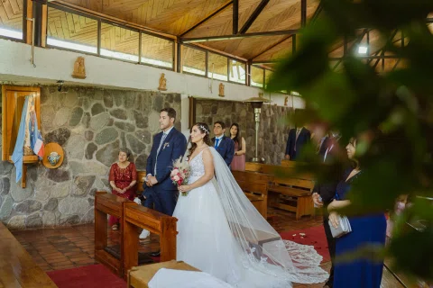 Hombre con traje azul y mujer con vestido blanco permanecen de pie junto a un reclinatorio dentro de la iglesia.