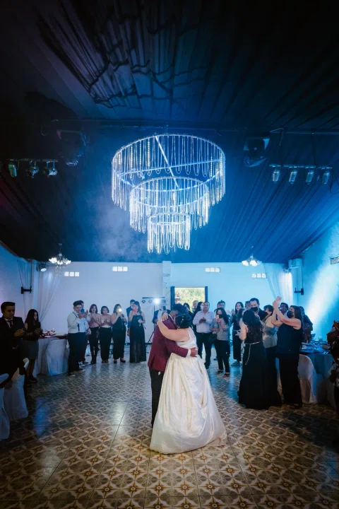 Hombre con traje burdeos y mujer con vestido blanco están en una pista de baile bajo iluminación azul.