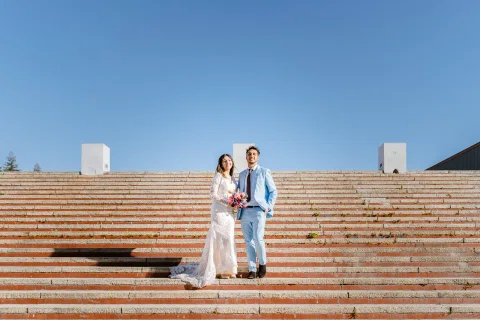 Hombre con traje celeste y mujer con vestido blanco están de pie sobre una amplia escalinata exterior.