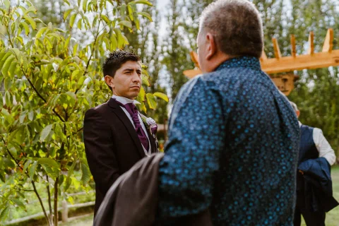 Hombre con traje oscuro conversa con otro hombre en el jardín.