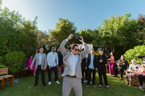 Hombre con traje gris levanta un objeto rectangular negro sobre la cabeza frente a un grupo de hombres.