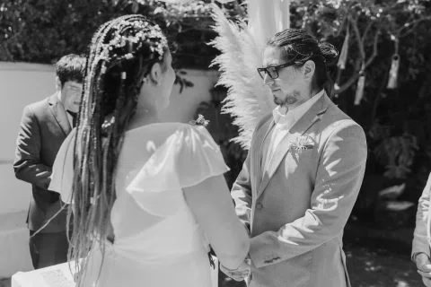 Hombre con traje gris y mujer con vestido blanco se besan en un primer plano en blanco y negro.