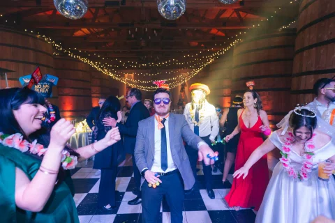 Hombre con traje y lentes oscuros baila en el centro de un grupo dentro del salón.
