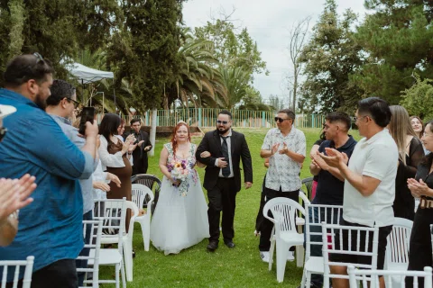 Hombre con traje negro y mujer con vestido floral caminan entre personas que aplauden.
