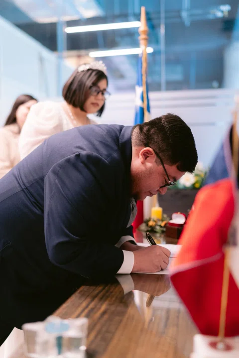Hombre con traje oscuro escribe sobre un documento en una mesa.