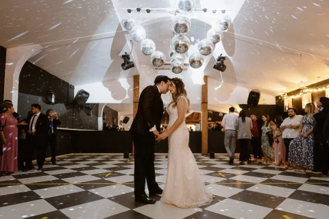 Hombre con traje oscuro y mujer con vestido blanco están juntos sobre una pista de cuadros blancos y negros.