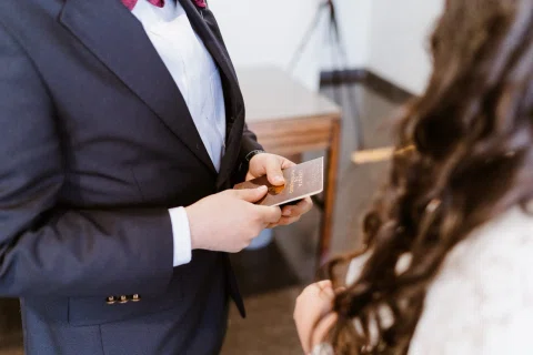 Hombre con traje oscuro sostiene una libreta con el texto “Libreta de Matrimonio” frente a una mujer.