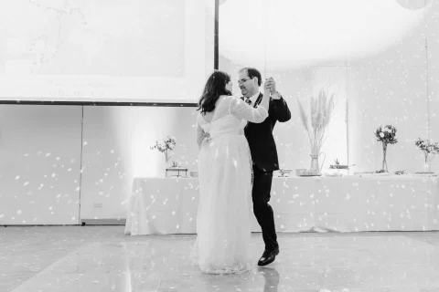 Hombre con traje oscuro y mujer con vestido blanco bailan juntos en una fotografía en blanco y negro.