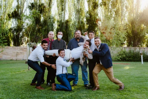Hombre con traje rayado es levantado horizontalmente por siete hombres sobre el césped durante una pose grupal.