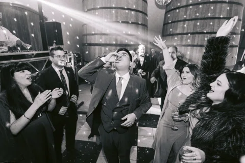 Hombre con traje y varias personas celebran en la pista mientras objetos vuelan por el aire, en blanco y negro.