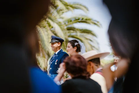 Hombre con uniforme azul y mujer con vestido blanco permanecen frente a frente entre varias personas.