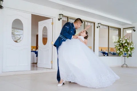 Hombre con uniforme azul inclina hacia atrás a una mujer con vestido blanco durante un baile.