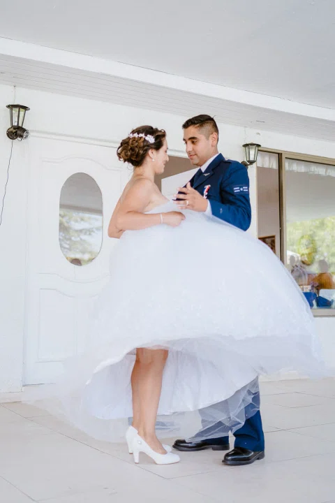 Hombre con uniforme azul y mujer con vestido blanco bailan juntos en un espacio interior luminoso.