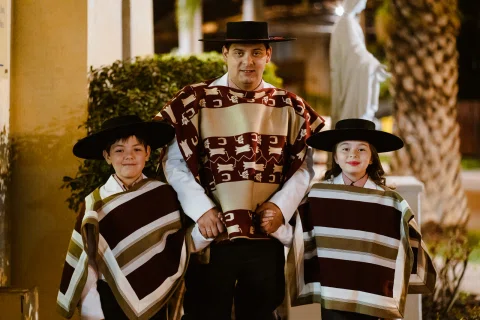 Hombre y dos niños con atuendos tradicionales posando frente a la entrada de una iglesia.