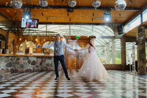 Hombre y mujer bailan juntos sobre un piso de cuadros blancos y negros en un salón de madera.