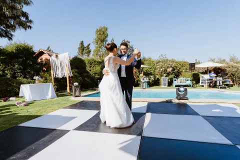 Hombre y mujer bailan sobre una pista de cuadros blancos y negros junto a la piscina.
