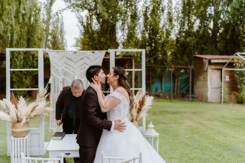 Hombre y mujer se besan bajo un arco blanco al aire libre.