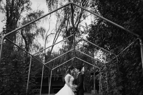 Hombre y mujer se besan bajo una estructura metálica en una fotografía en blanco y negro.