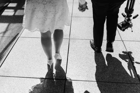 Fotografía en blanco y negro de un hombre y una mujer caminando juntos; él lleva una cámara en una mano.