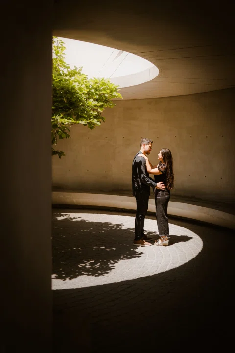 Hombre y mujer permanecen de pie dentro de una zona circular de luz en una estructura de hormigón.