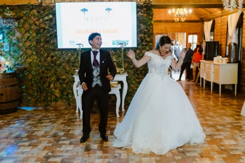 Hombre y mujer entran al salón con los brazos levantados mientras varias personas observan.